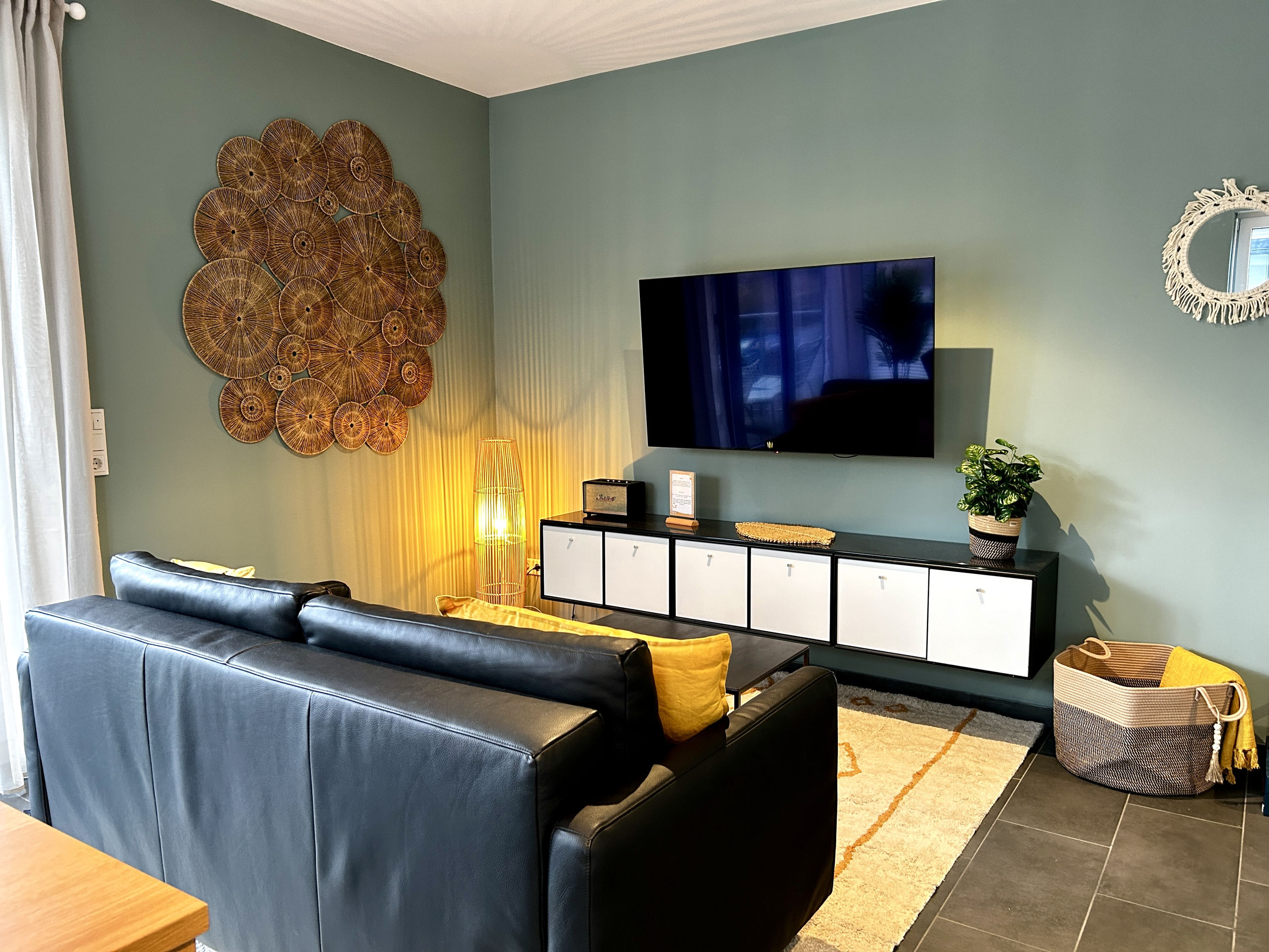 Media corner with wall-mounted TV, long sideboard with white cube doors, glowing rattan floor lamp, and sofa seen from behind.
