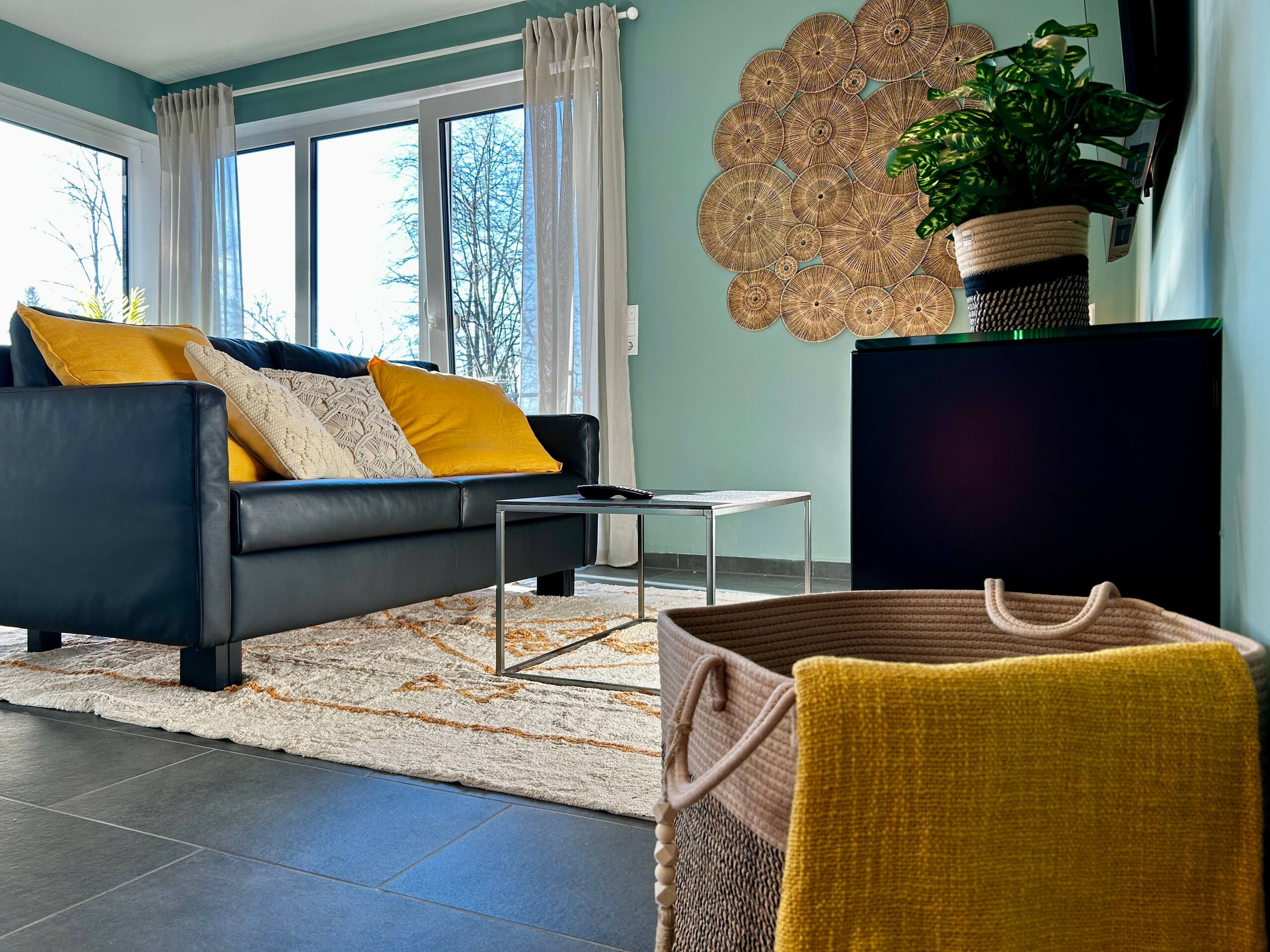 Low-angle detail of the sofa corner with yellow and cream cushions, slim coffee table, patterned rug, and a woven basket with throw.