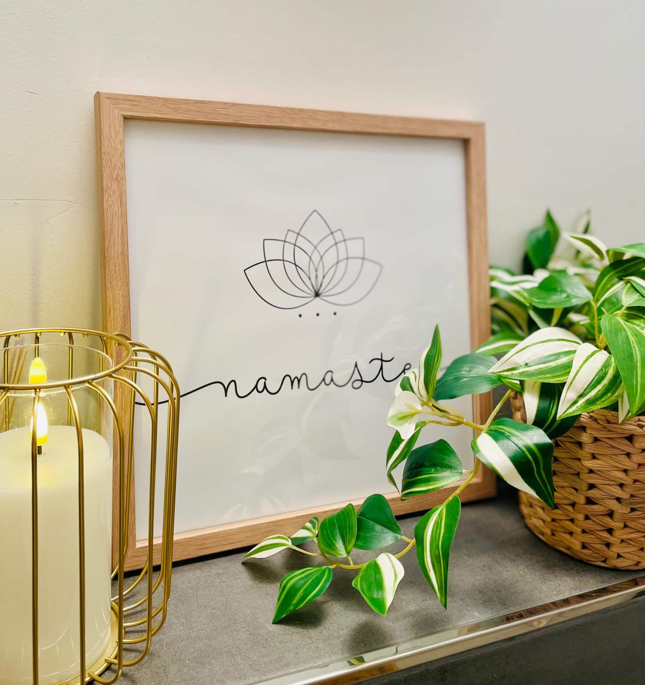 Decor detail with a framed lotus print reading namaste, a lit candle in a gold wire holder, and a variegated plant in a woven basket.