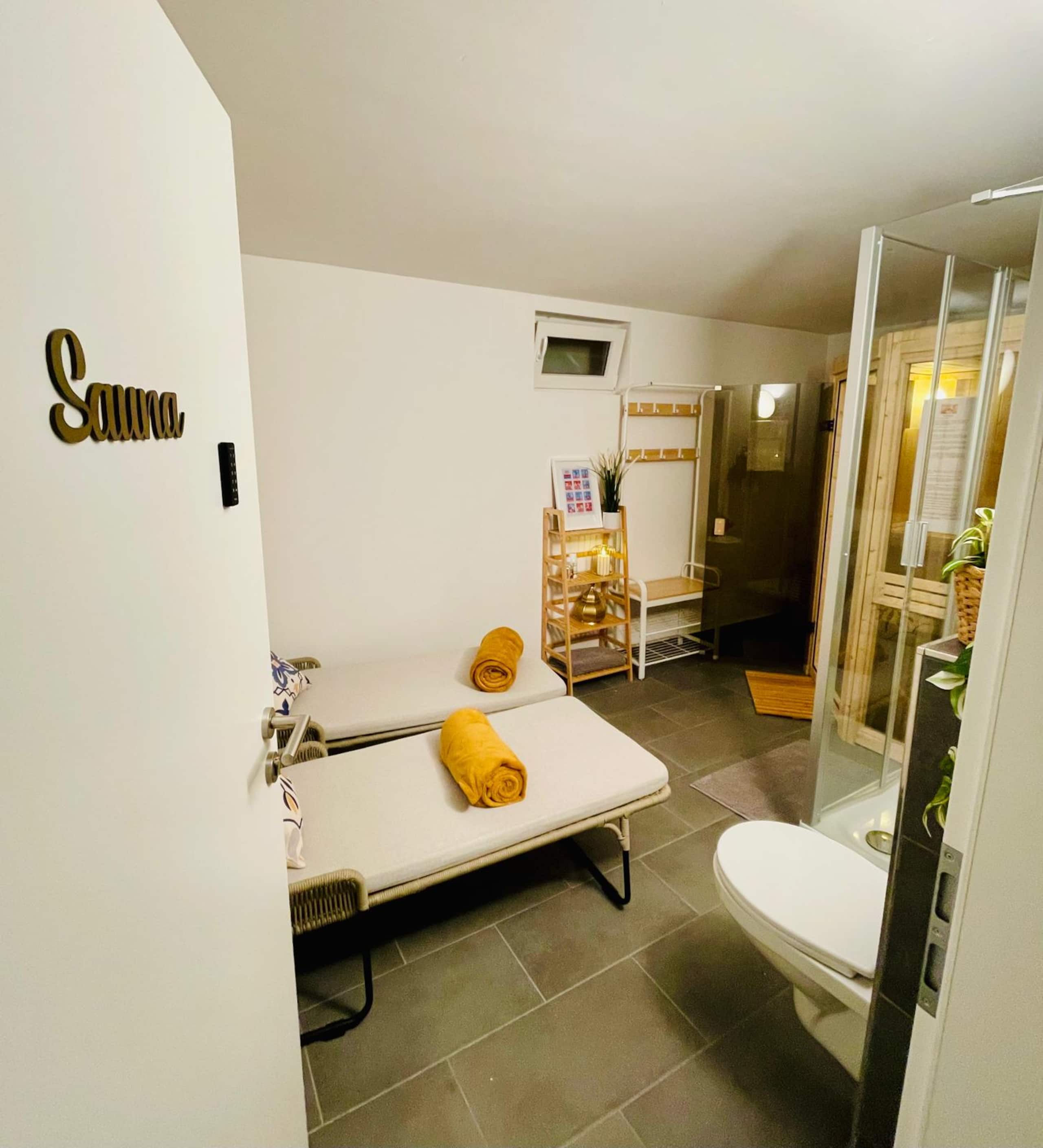 Relax room with two white loungers, a bamboo shelf, a coat rack, and the lit sauna cabin glowing on the right.