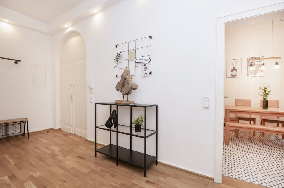 Helles Entrée mit Parkett, Rundbogentür und schwarzem Konsolentisch, darüber ein Wandgitter mit Deko; rechts der Blick ins Esszimmer.