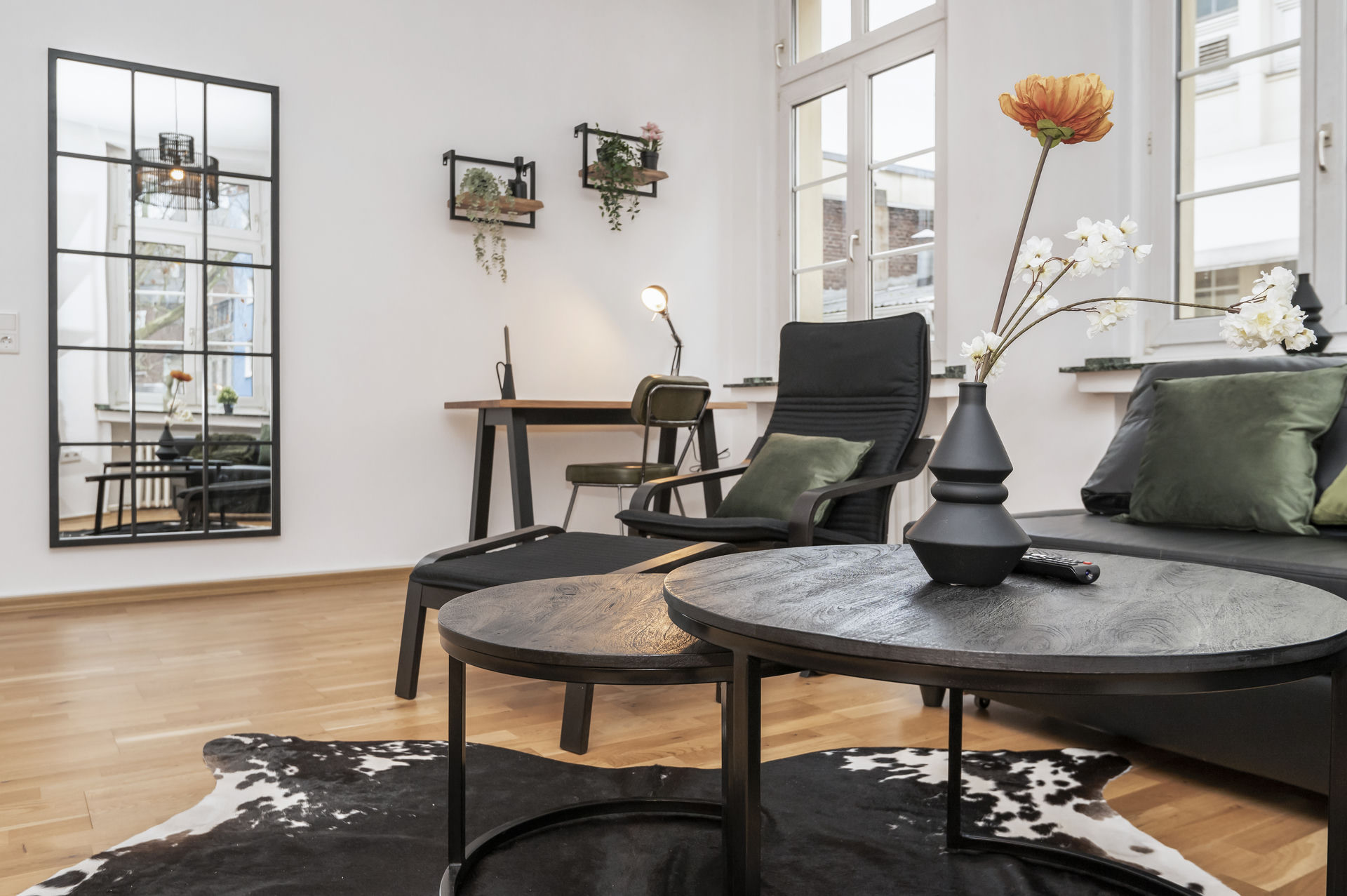 Low view of round black coffee tables with a vase of flowers, a lounge chair and a grid mirror leaning against the wall.