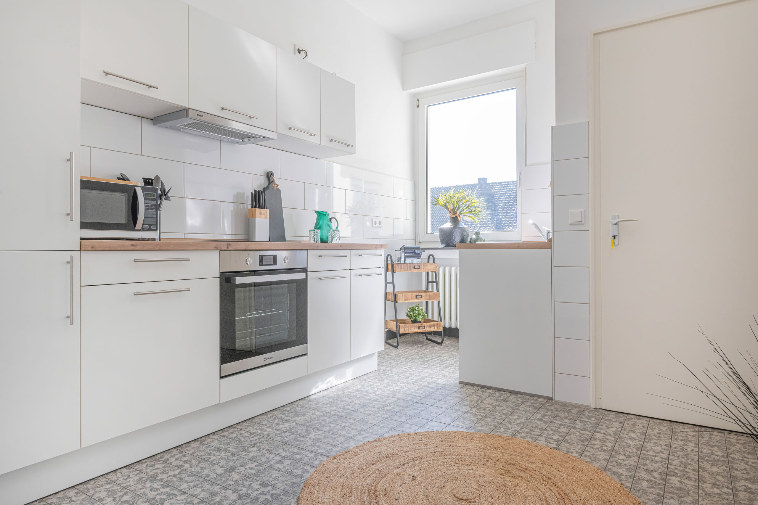 White kitchen with wooden worktops, a built-in oven, a microwave on the counter, glossy tiled splashback and patterned floor tiles.