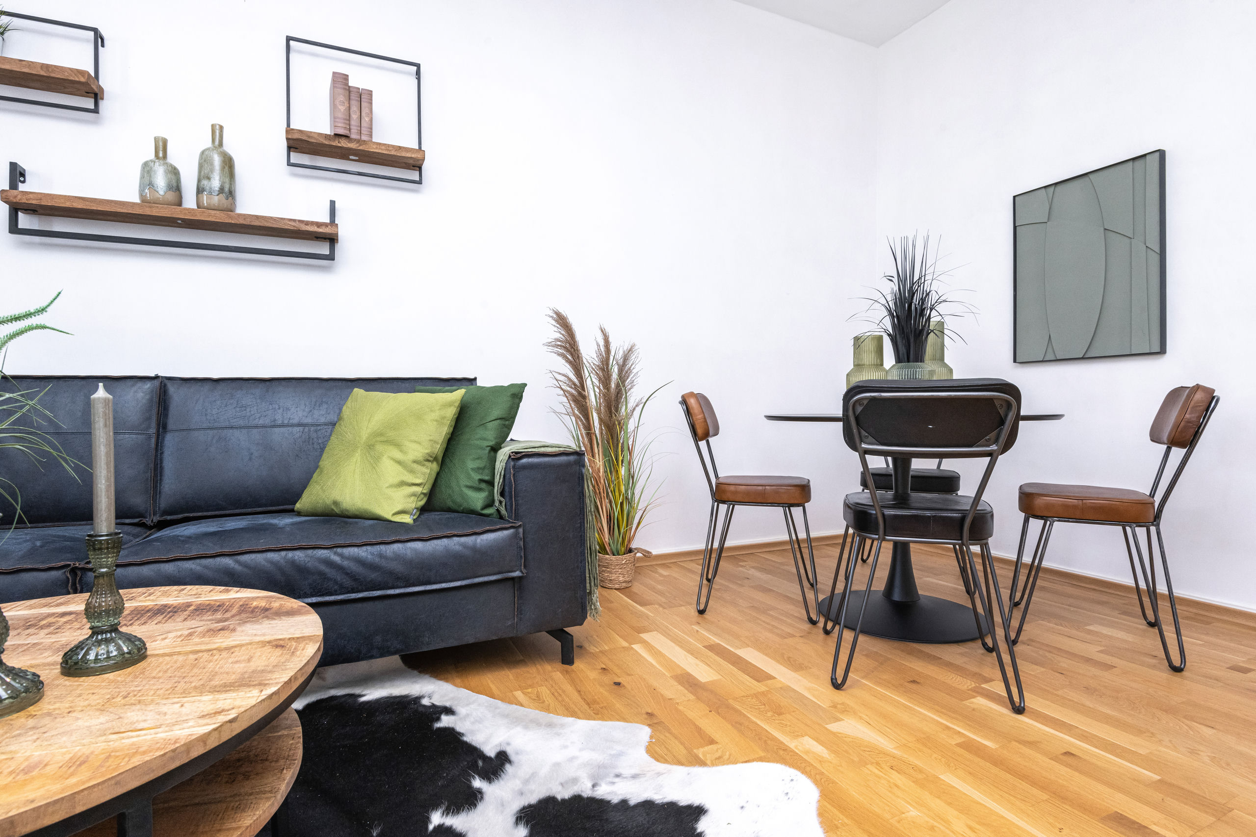 Sofa corner and dining nook with a round black table, three leather chairs and a framed wall panel on the white wall.