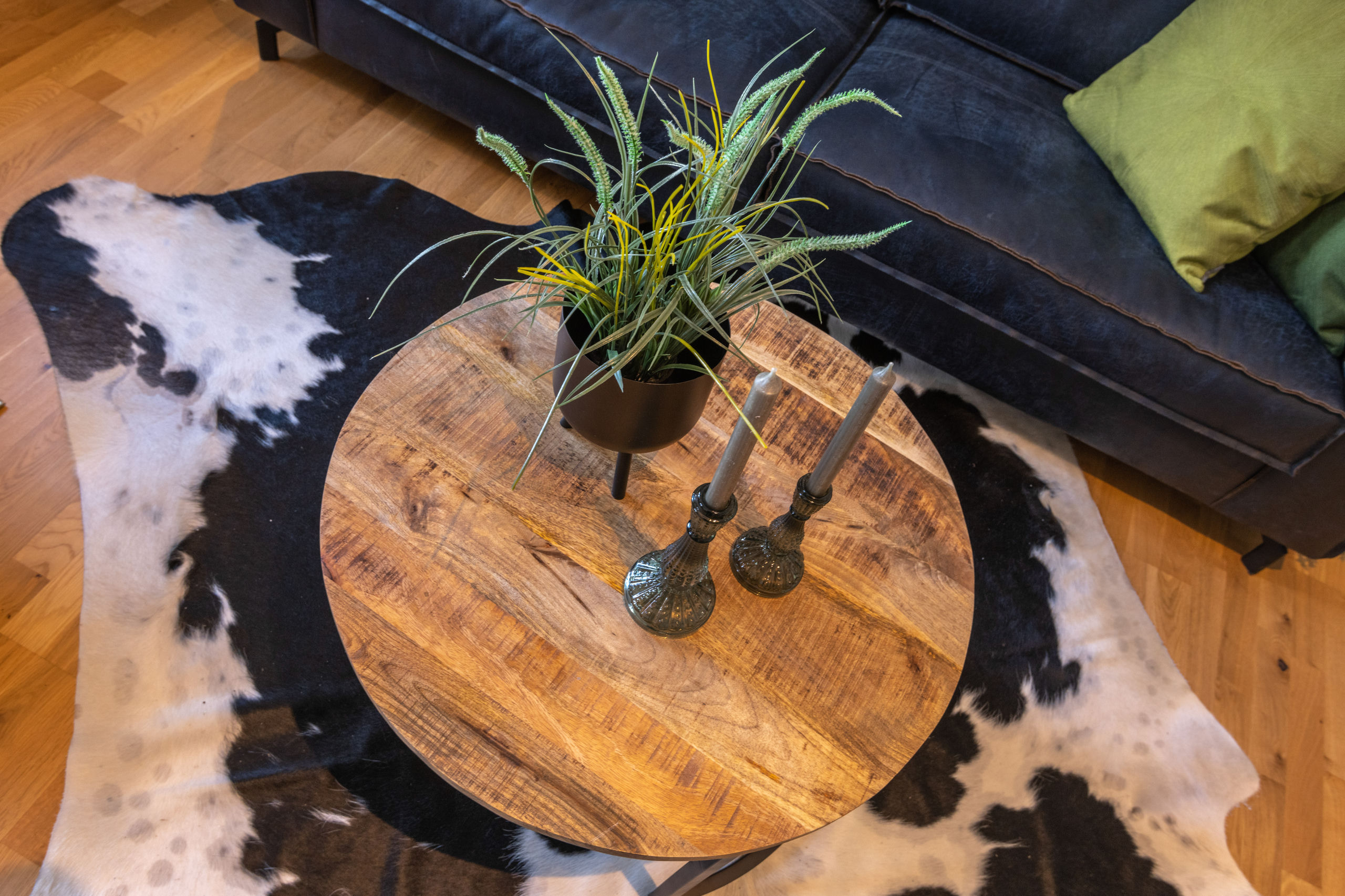 Overhead view of a round wooden coffee table with a potted plant and two candles, standing on a black and white cowhide rug.