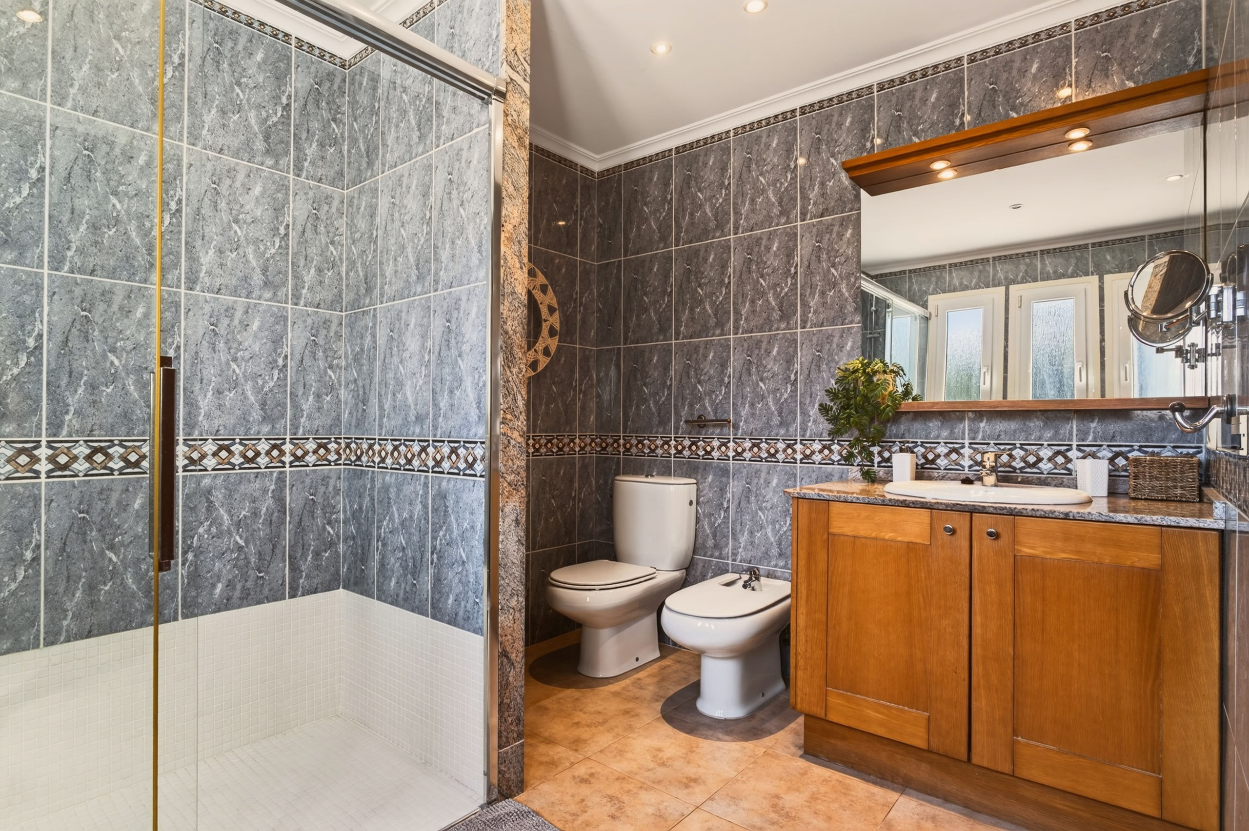 Zweiter Blickwinkel des Badezimmers mit grauen Marmorfliesen: Holzwaschtisch mit Spiegel, Toilette und Bidet neben der Duschkabine.
