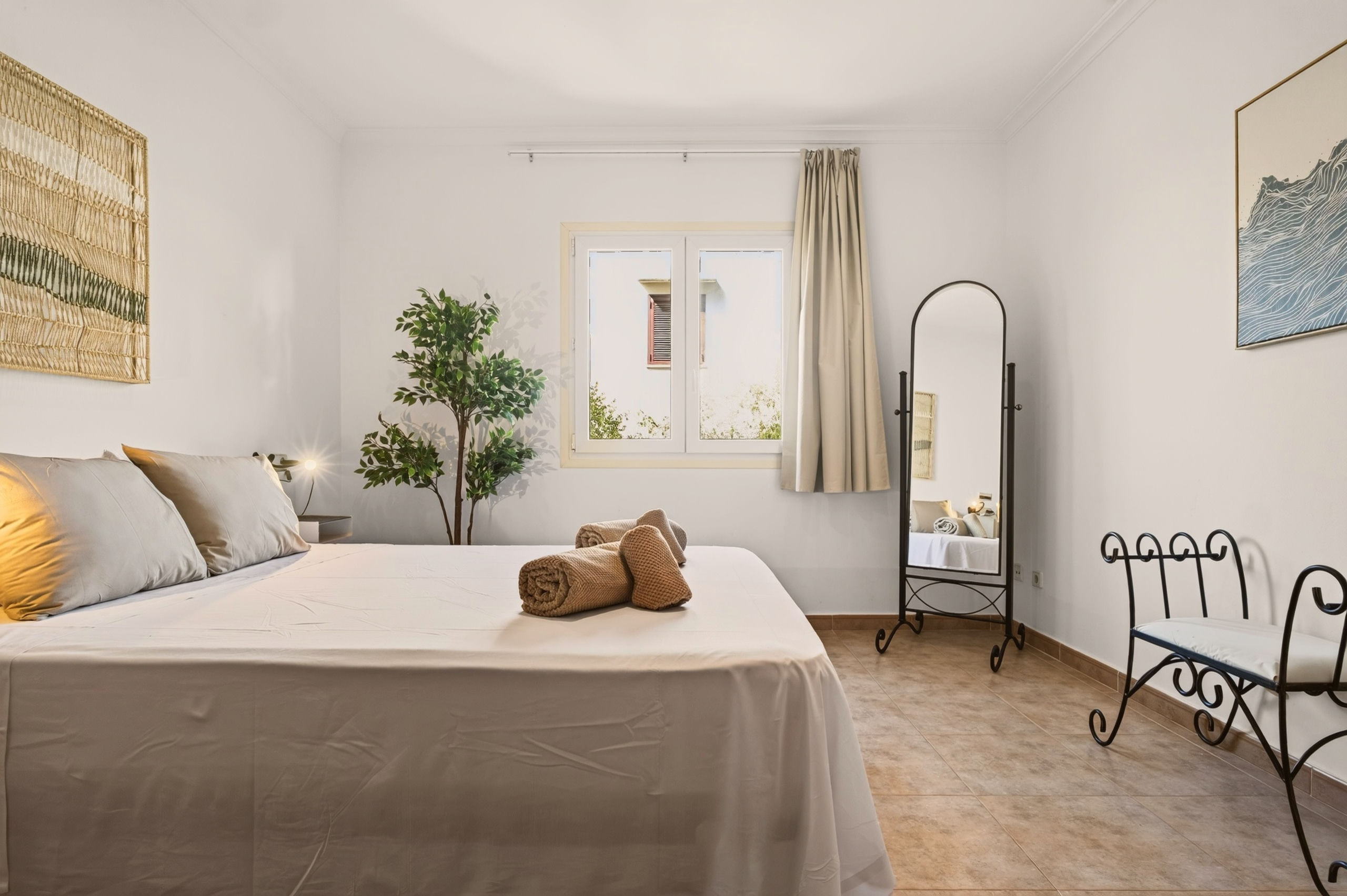 Weitere Ansicht des Schlafzimmers mit grauem Bett: Fenster, Standspiegel mit Bogen, gerahntes Wellenbild und Schmiedeeisenbank.
