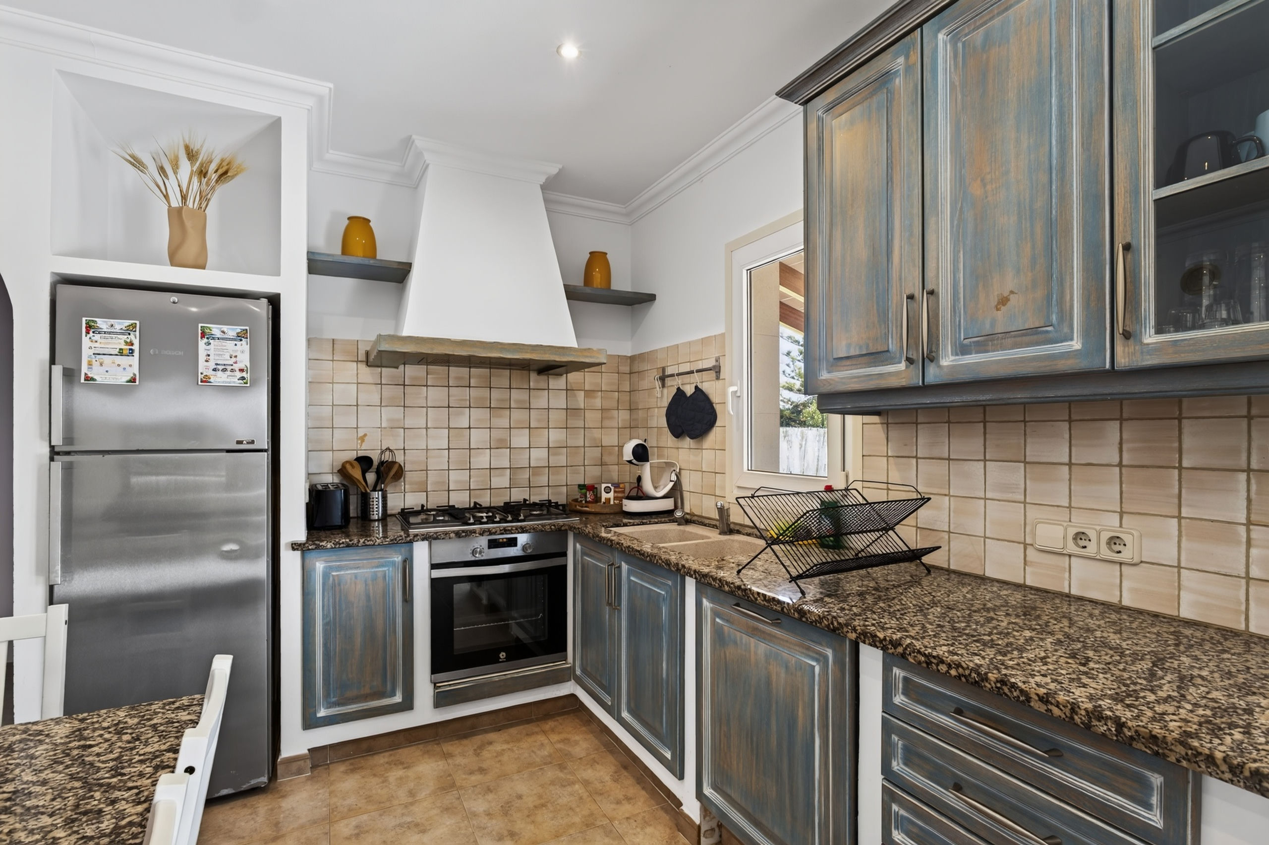 Arbeitsecke mit Gaskochfeld, eingebautem Backofen, Spüle mit Abtropfregal, blauen Fronten und Glas-Oberschränken darüber.